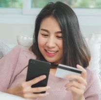 <p>Young smiling Asian woman using smartphone buying online shopping by credit card while lying on sofa when relax in living room at home. Lifestyle latin and hispanic ethnicity women at house concept.</p>