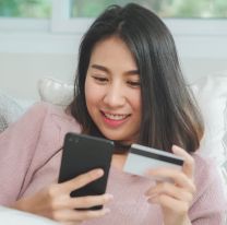 <p>Young smiling Asian woman using smartphone buying online shopping by credit card while lying on sofa when relax in living room at home. Lifestyle latin and hispanic ethnicity women at house concept.</p>
